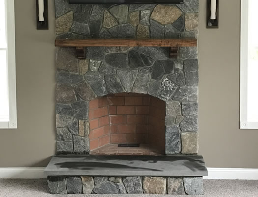 After: floor-to-ceiling natural stone fireplace makeover with a timber beam mantle in Lunenburg MA